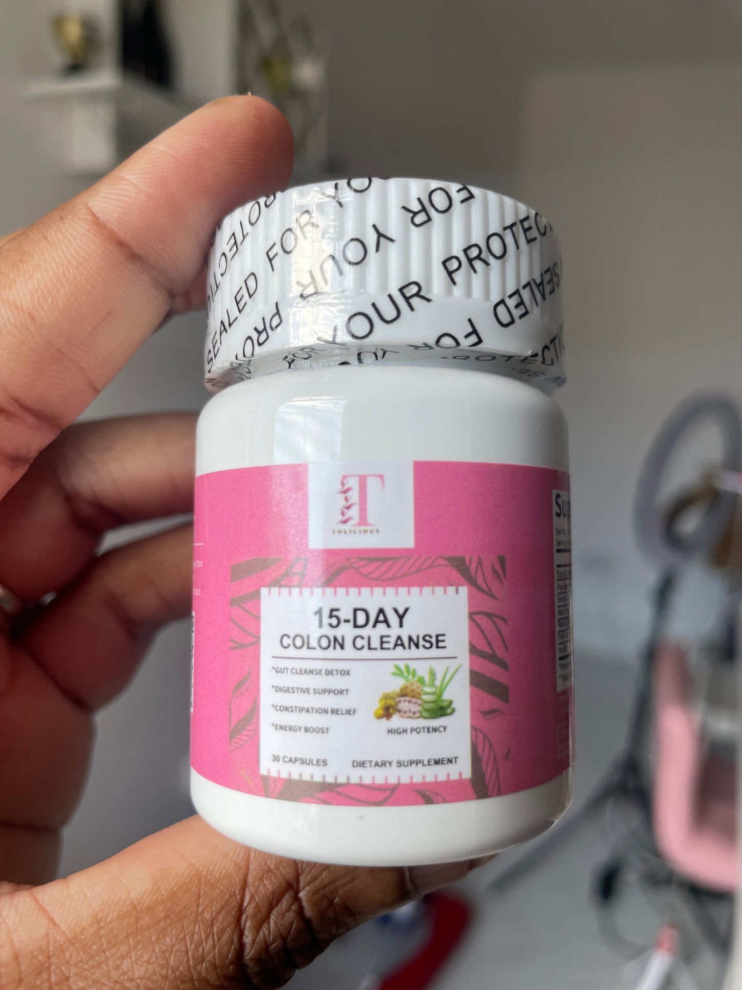 Hand holding a '15-Day Colon Cleanse' supplement bottle with a pink label.